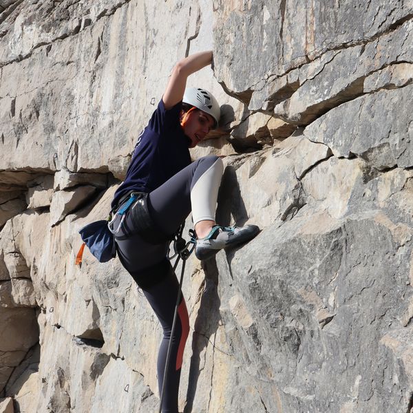 A woman on a the crux of a route with her foot placed at waist height